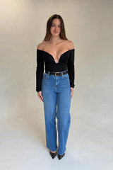 A young woman wears the Renee Leather Belt Black Croc with a black off-shoulder top, high-rise jeans, and pointed-toe mesh heels.
