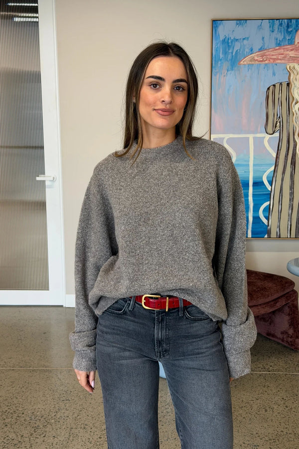 A young woman wears a red Renee Leather Belt Croc with a gold buckle, paired with a grey knit sweater and charcoal jeans.