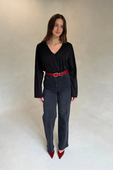 A woman wears a black V-neck top and charcoal jeans, accessorized with a red croc-embossed Renee Leather Belt and matching heels.