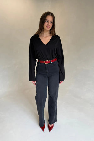 A woman wears a black V-neck top and charcoal jeans, accessorized with a red croc-embossed Renee Leather Belt and matching heels.