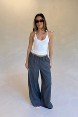 A woman wears Zoe Relaxed Suit Pant Grey with a white racerback tank, black sunglasses, gold jewelry, and red nail polish.