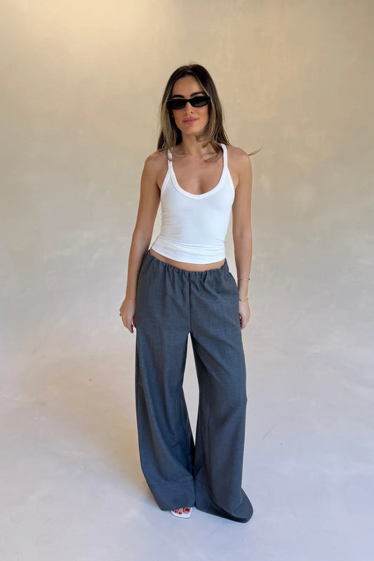 A woman wears Zoe Relaxed Suit Pant Grey with a white racerback tank, black sunglasses, gold jewelry, and red nail polish.