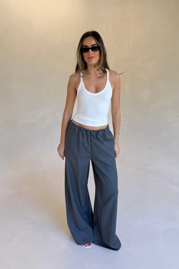 A woman wears Zoe Relaxed Suit Pant Grey with a white racerback tank, black sunglasses, gold jewelry, and red nail polish.