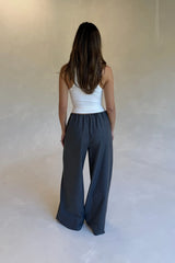 A woman stands facing away wearing a white halter tank and Zoe Relaxed Suit Pant Grey wide-leg trousers in a minimalist studio.